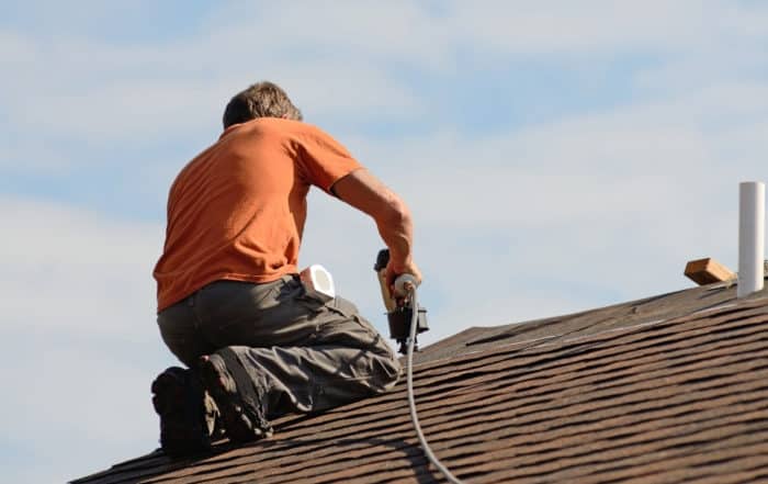 roofing contractor kneeling on roof repairing damages