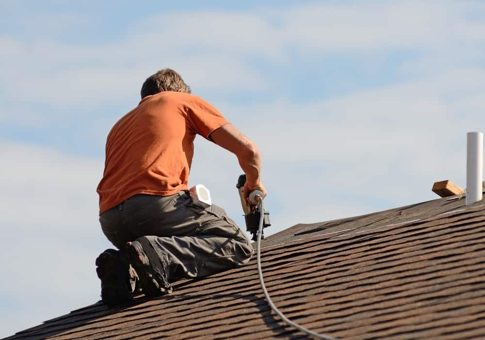 roofing contractor kneeling on roof repairing damages